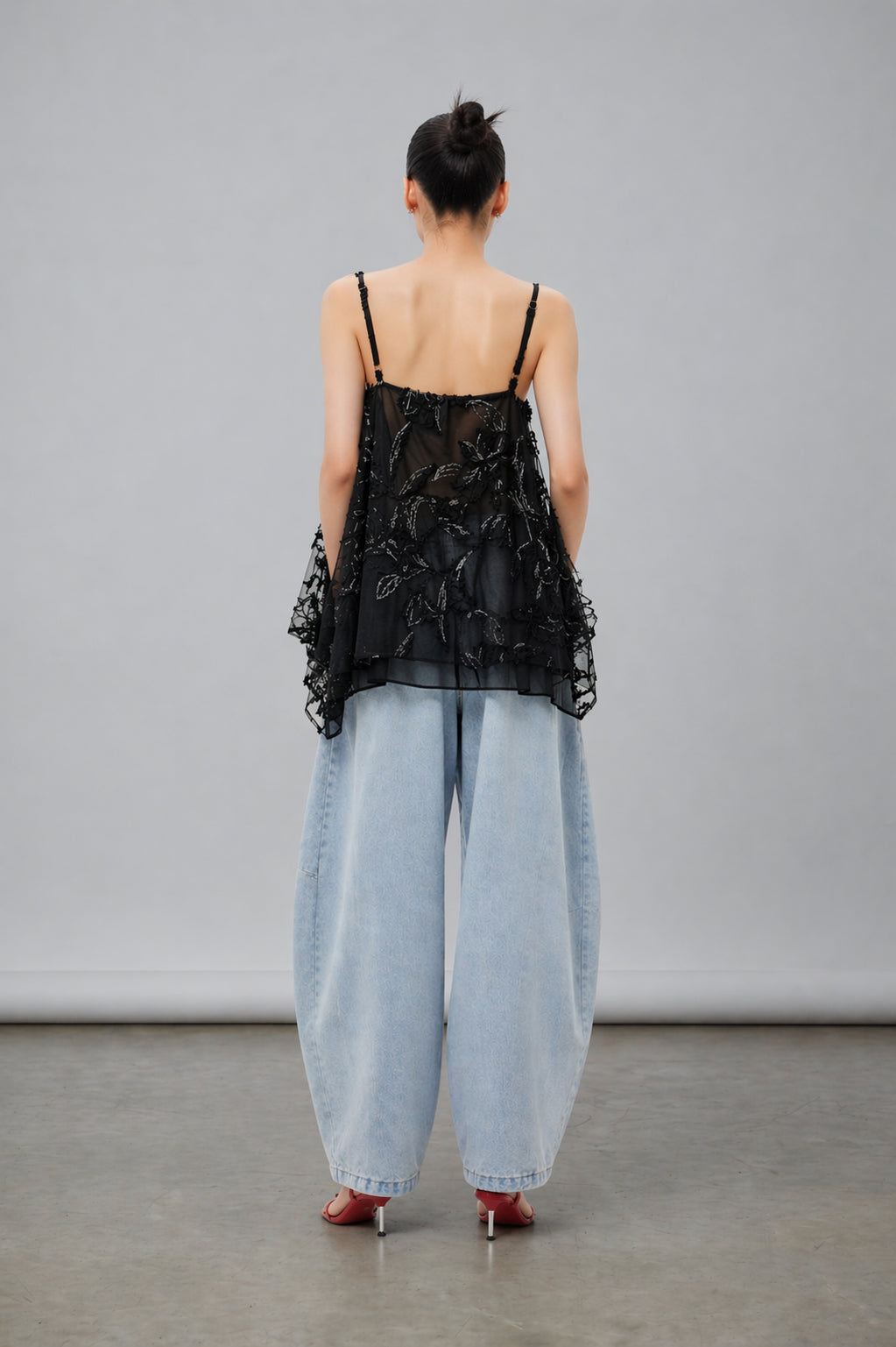 Singapore woman wearing a black lace top and light blue jeans against a gray background