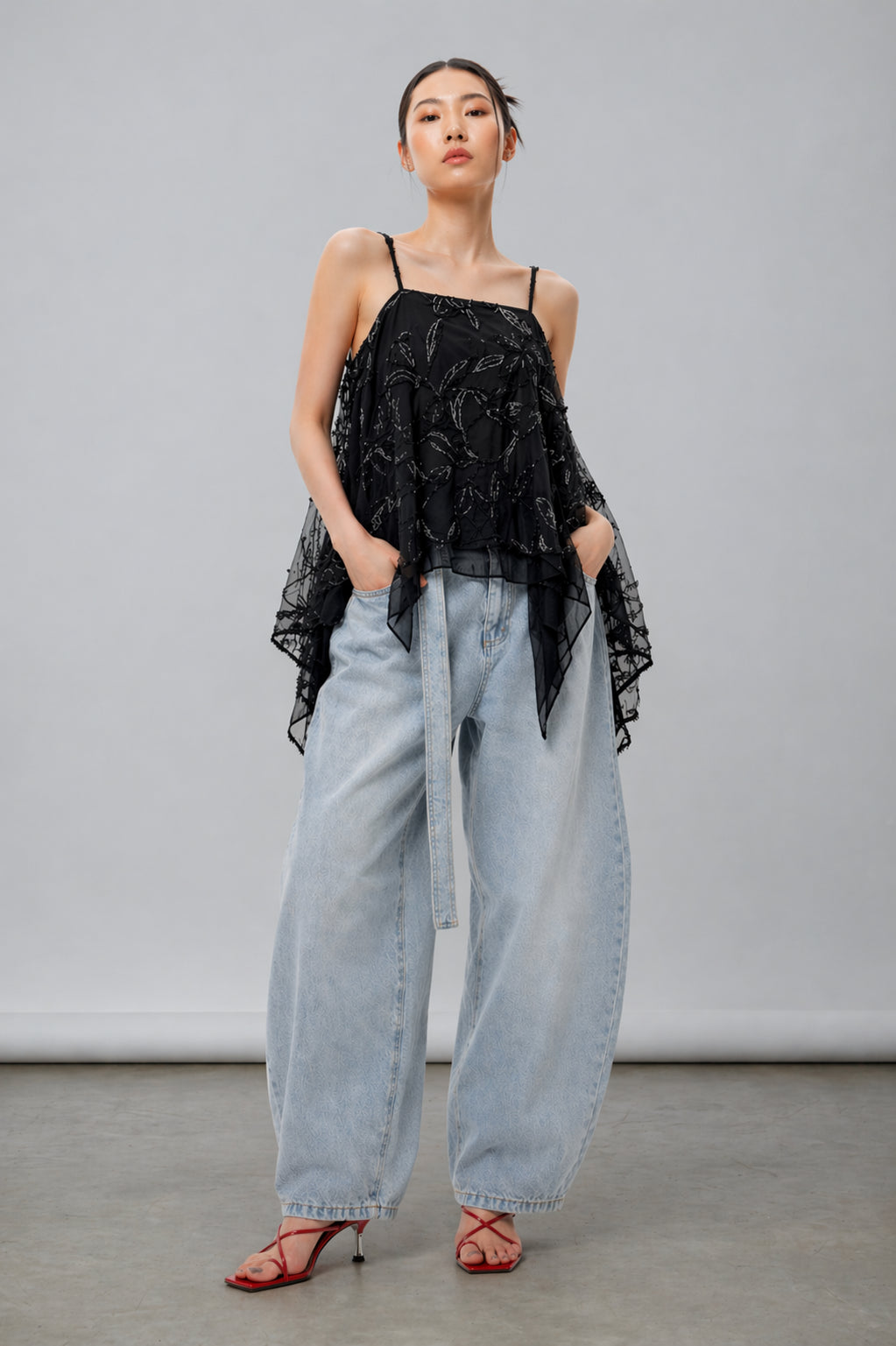 SIngapore Woman wearing a black lace top and light blue jeans against a gray background