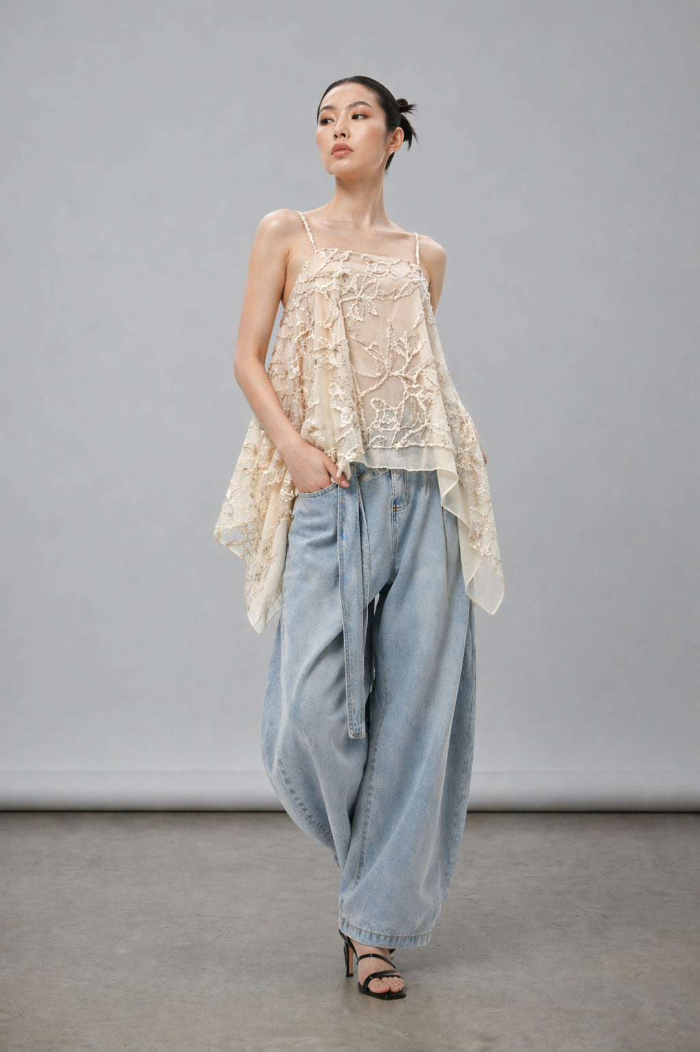 Asian Model wearing a beige lace top and light blue pants against a gray background