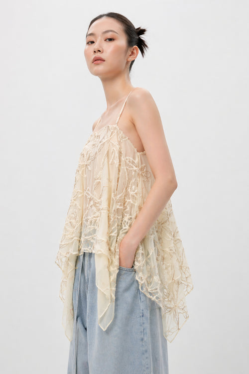 Woman wearing a light-colored lace top and denim pants against a plain background