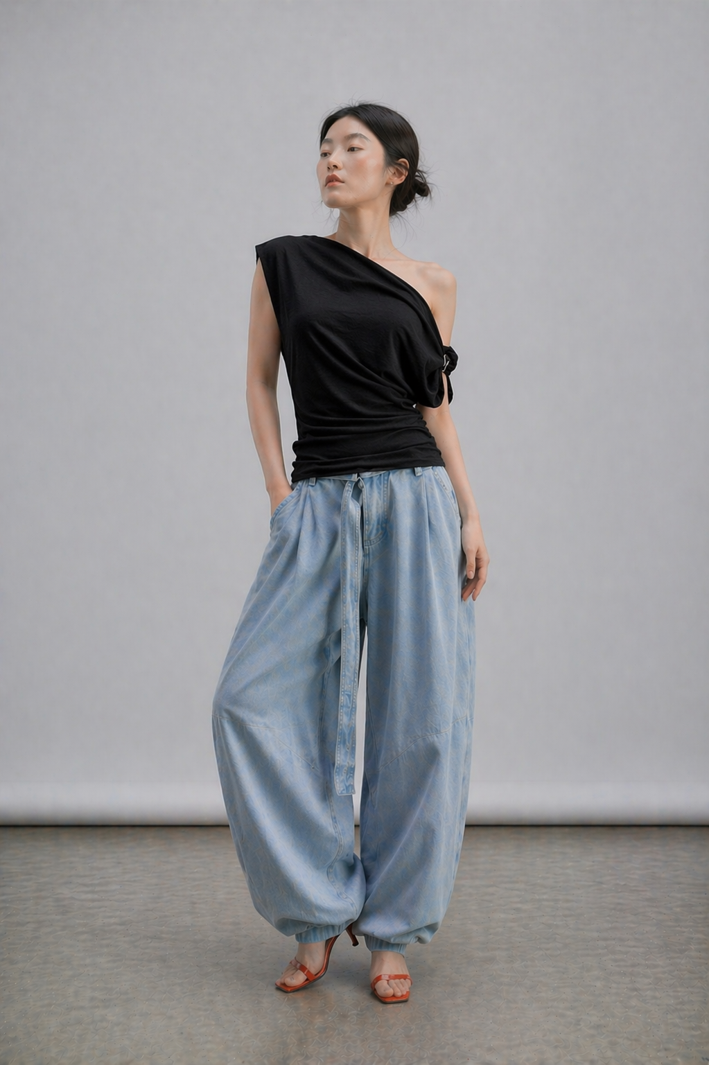 Woman wearing a black one-shoulder top and light blue wide-leg pants against a plain background