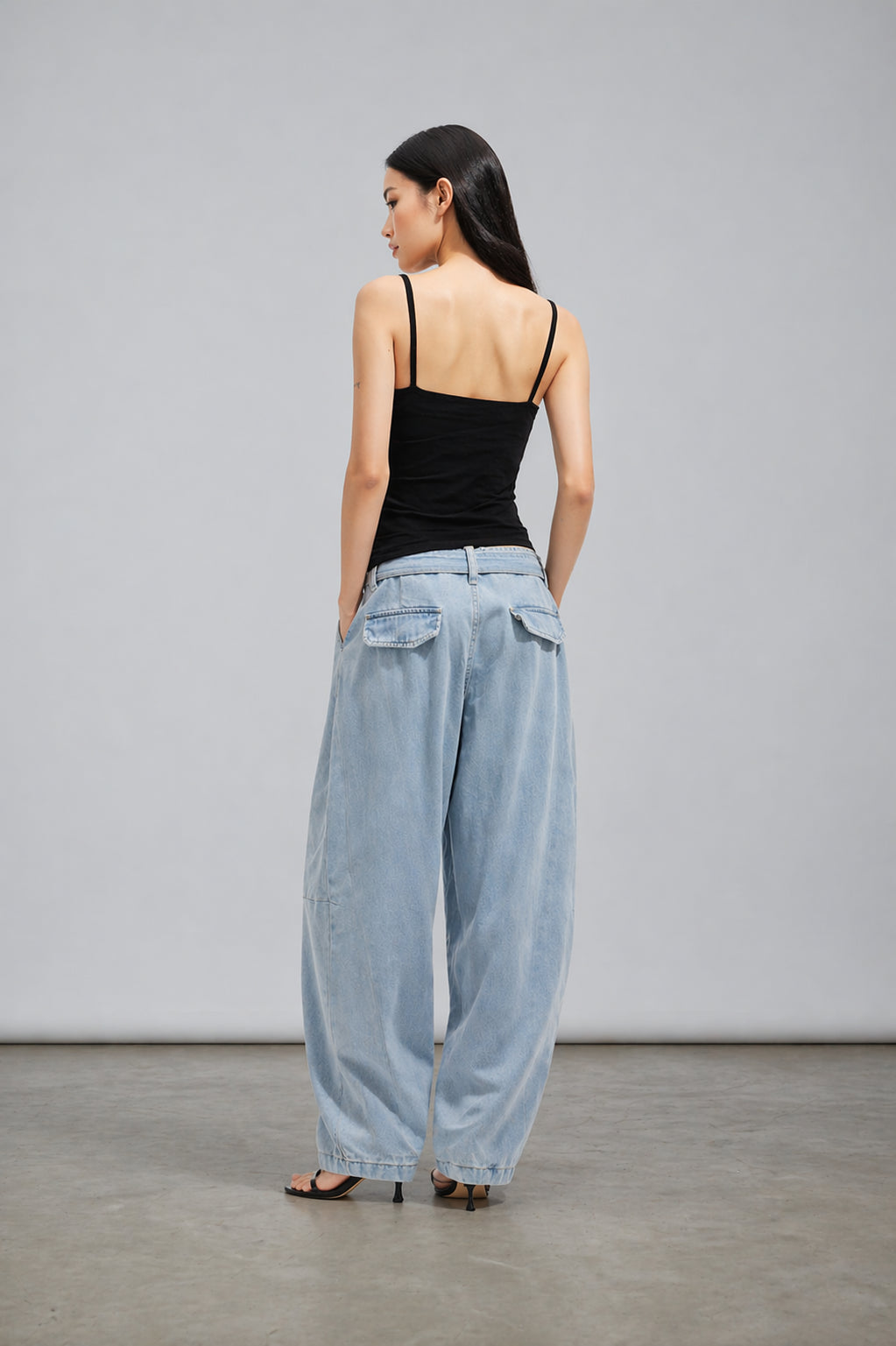 Woman wearing a black top and light blue wide-leg pants against a gray background