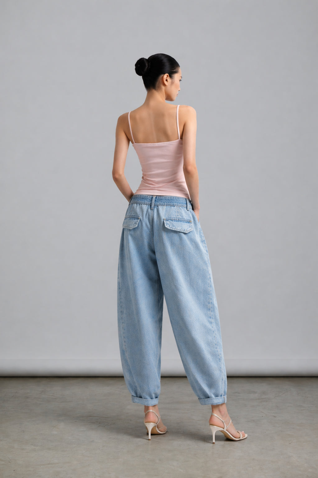 Woman wearing a pink top and light blue jeans against a gray background