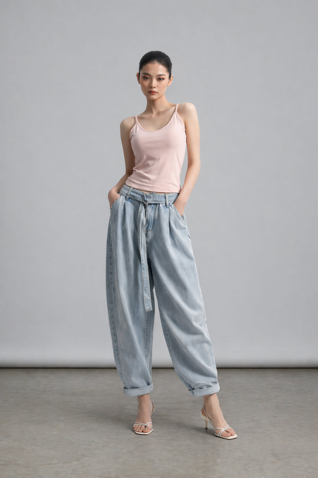 Woman wearing a pink tank top and light blue pants against a gray background