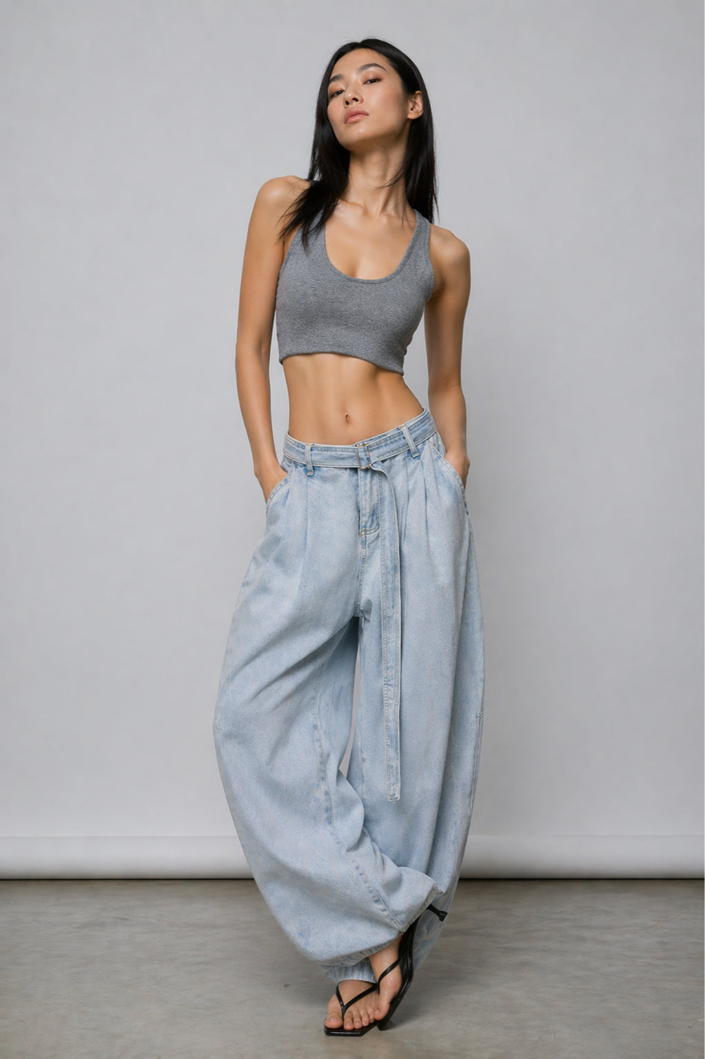 Woman wearing a gray crop top and light blue wide-leg pants against a plain background