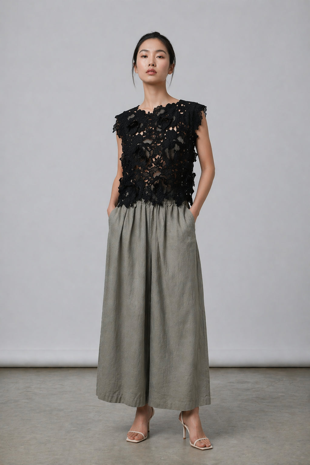 Woman wearing a black floral top and gray pants against a plain background