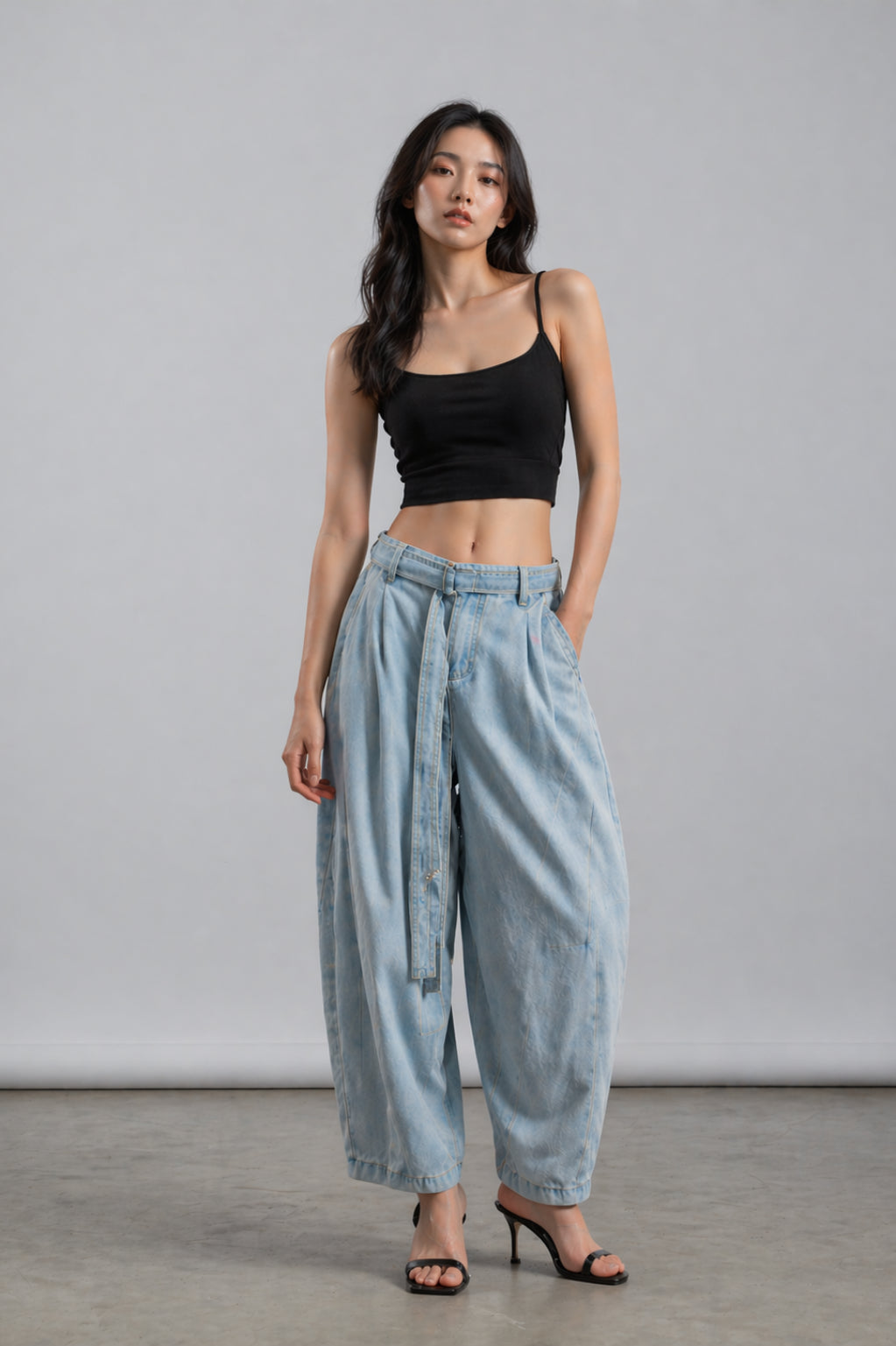 Woman wearing a black top and light blue denim pants against a gray background