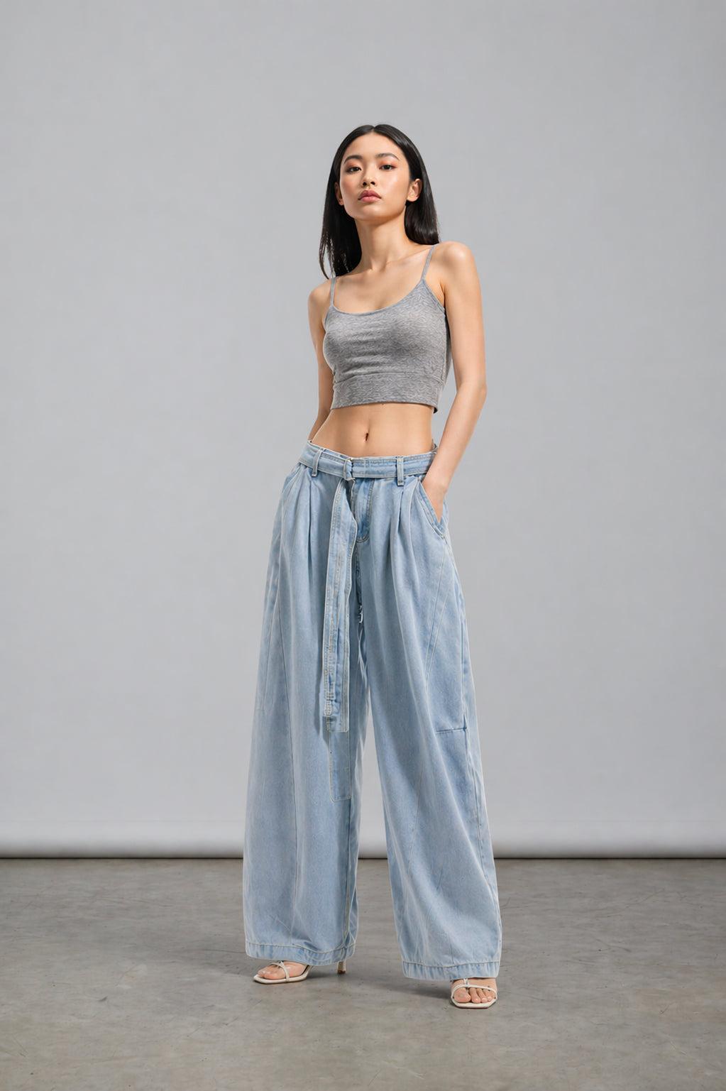 Woman wearing a gray tank top and light blue wide-leg pants against a plain background