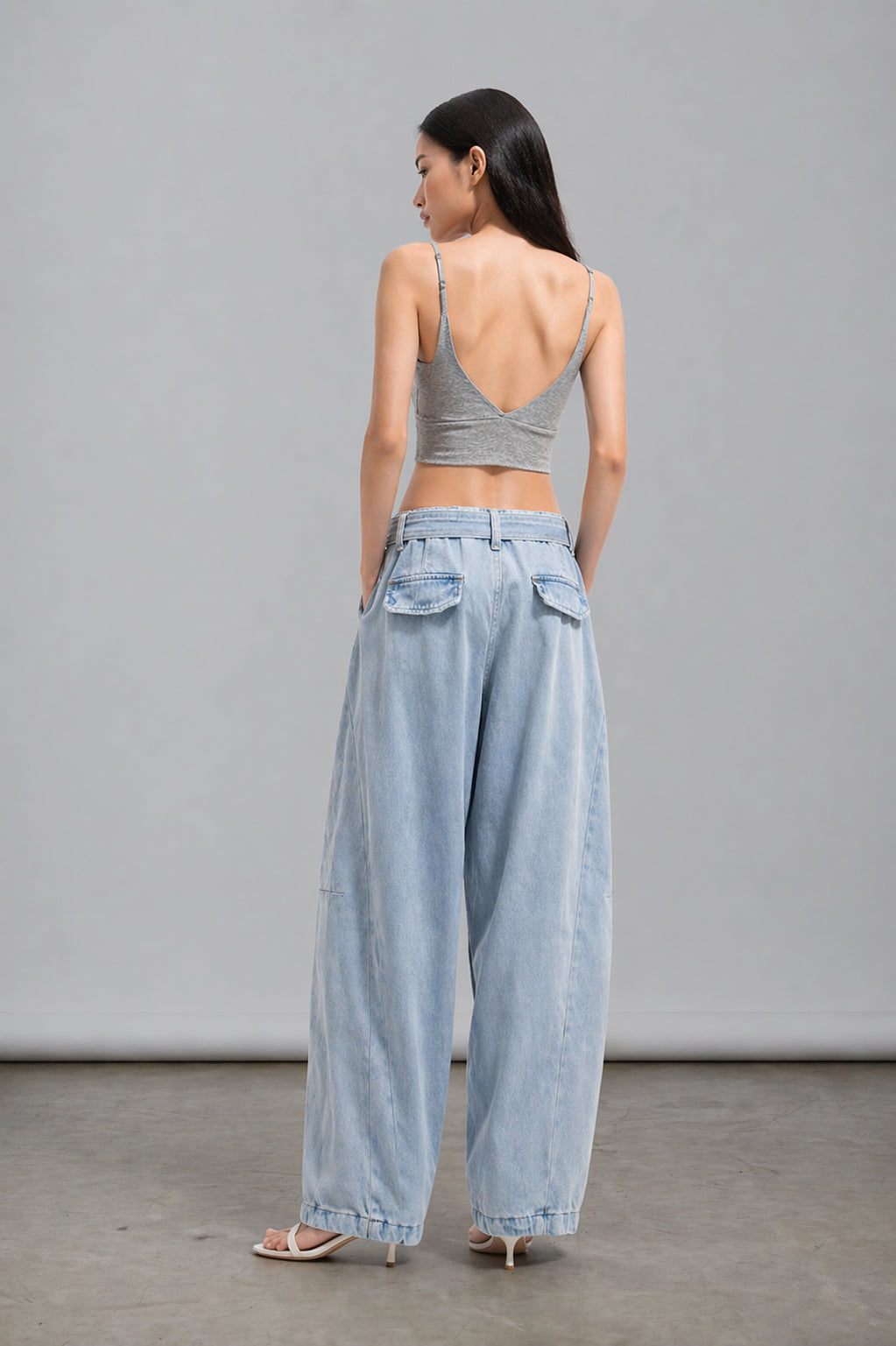Woman wearing a gray crop top and light blue wide-leg pants against a plain background
