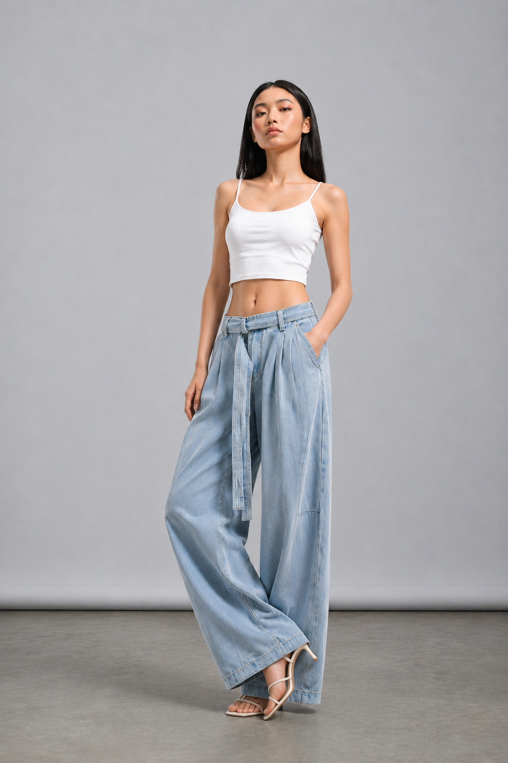 Woman wearing a white crop top and light blue wide-leg pants on a gray background