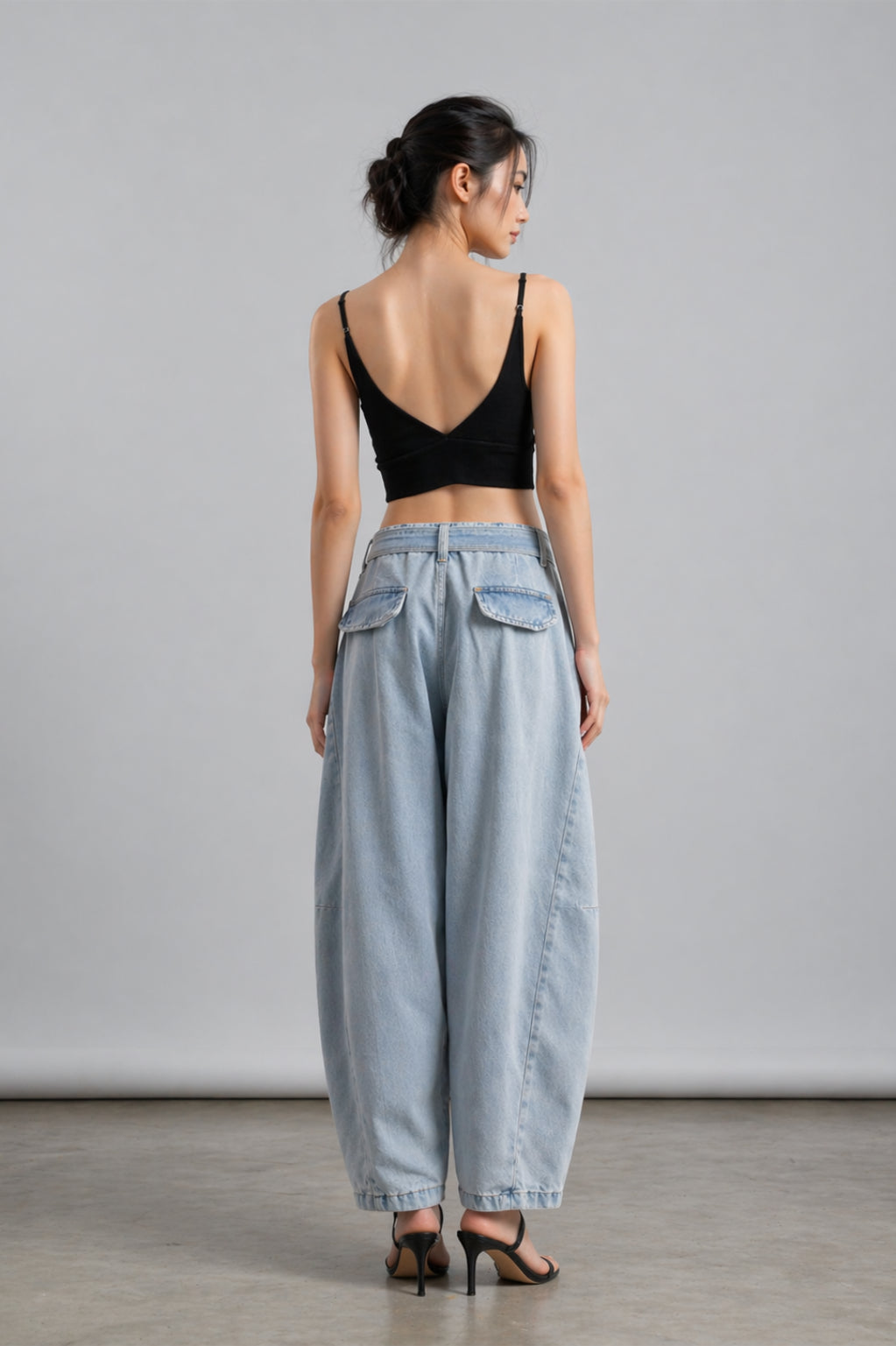 Woman wearing a black top and light blue jeans against a gray background