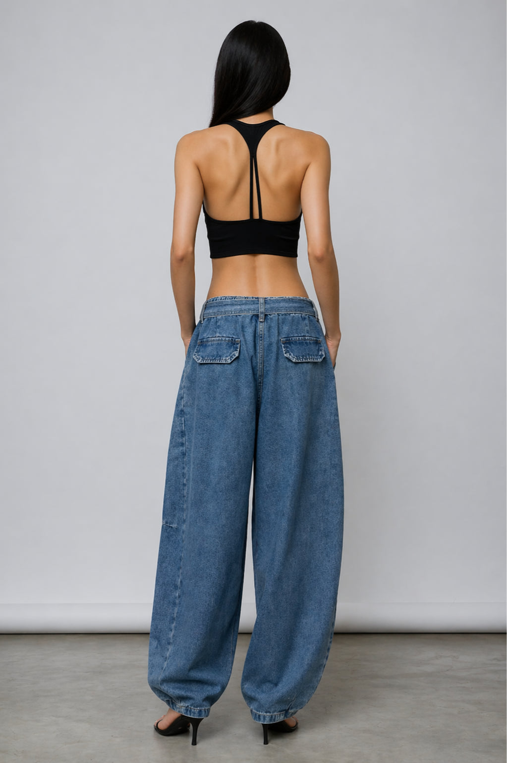 Person wearing a black bralette top and blue jeans from behind on a plain background