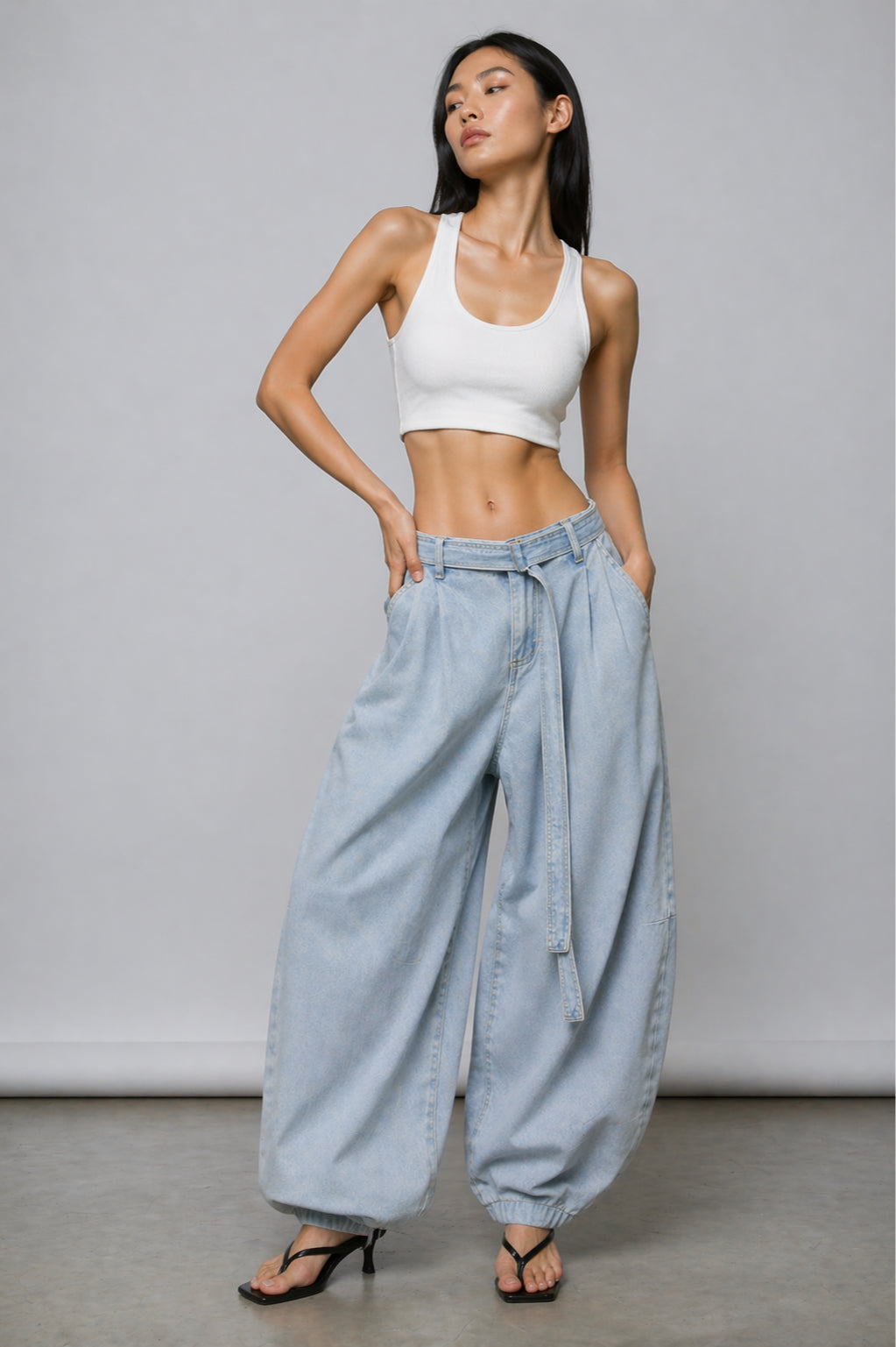 Woman wearing a white crop top and light blue jeans against a gray background