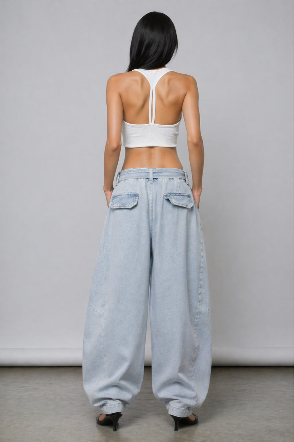 Person wearing a white crop top and light blue jeans against a plain background
