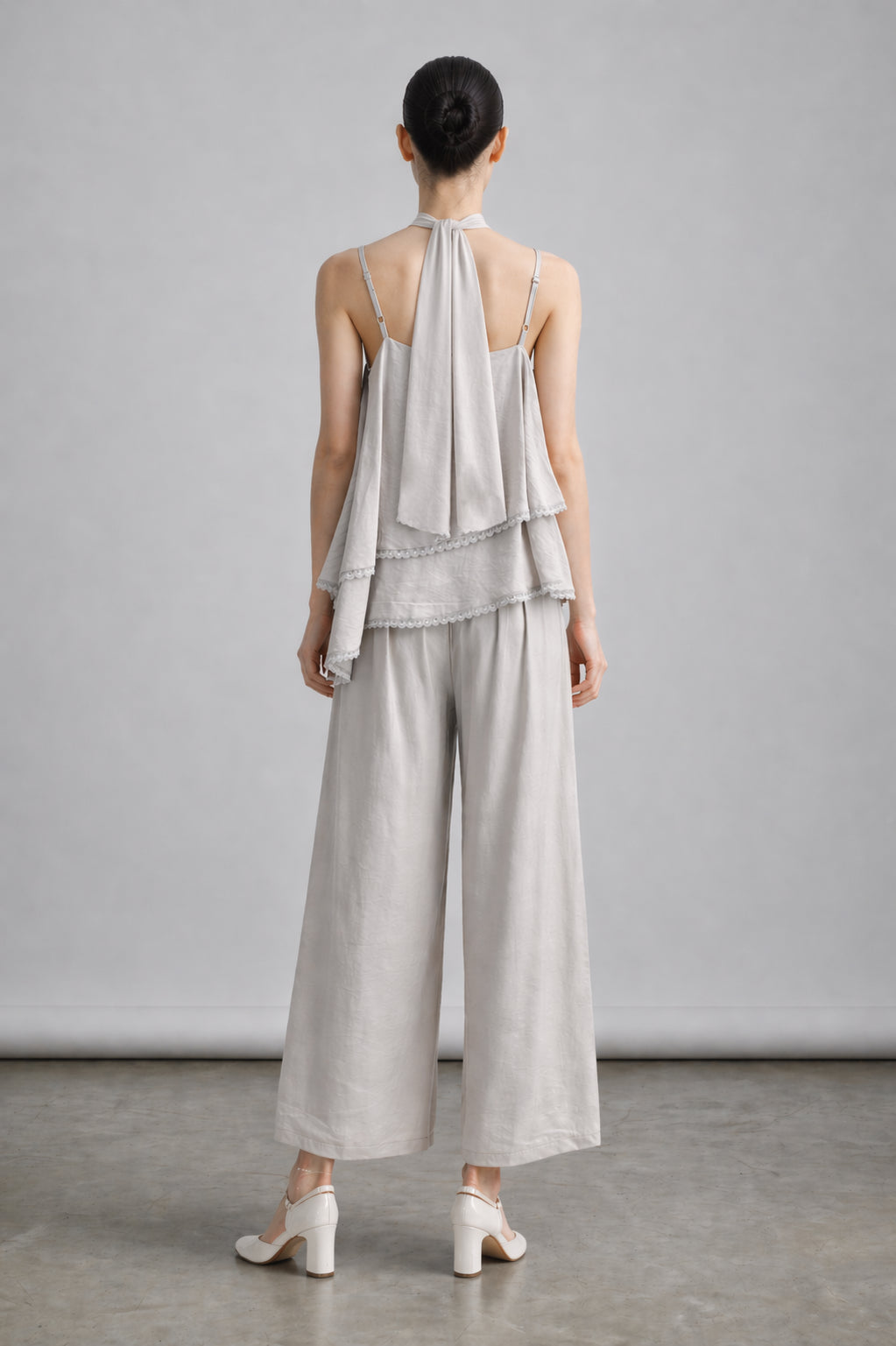 Woman wearing a light gray halter top and wide-leg pants against a plain background