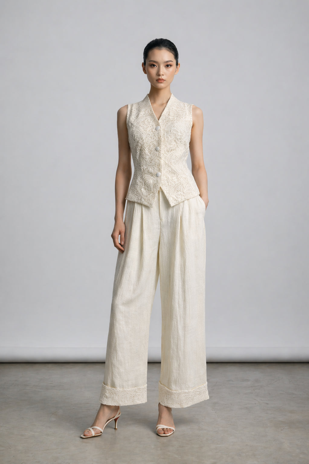Woman wearing a sleeveless beige top and wide-leg pants against a plain background