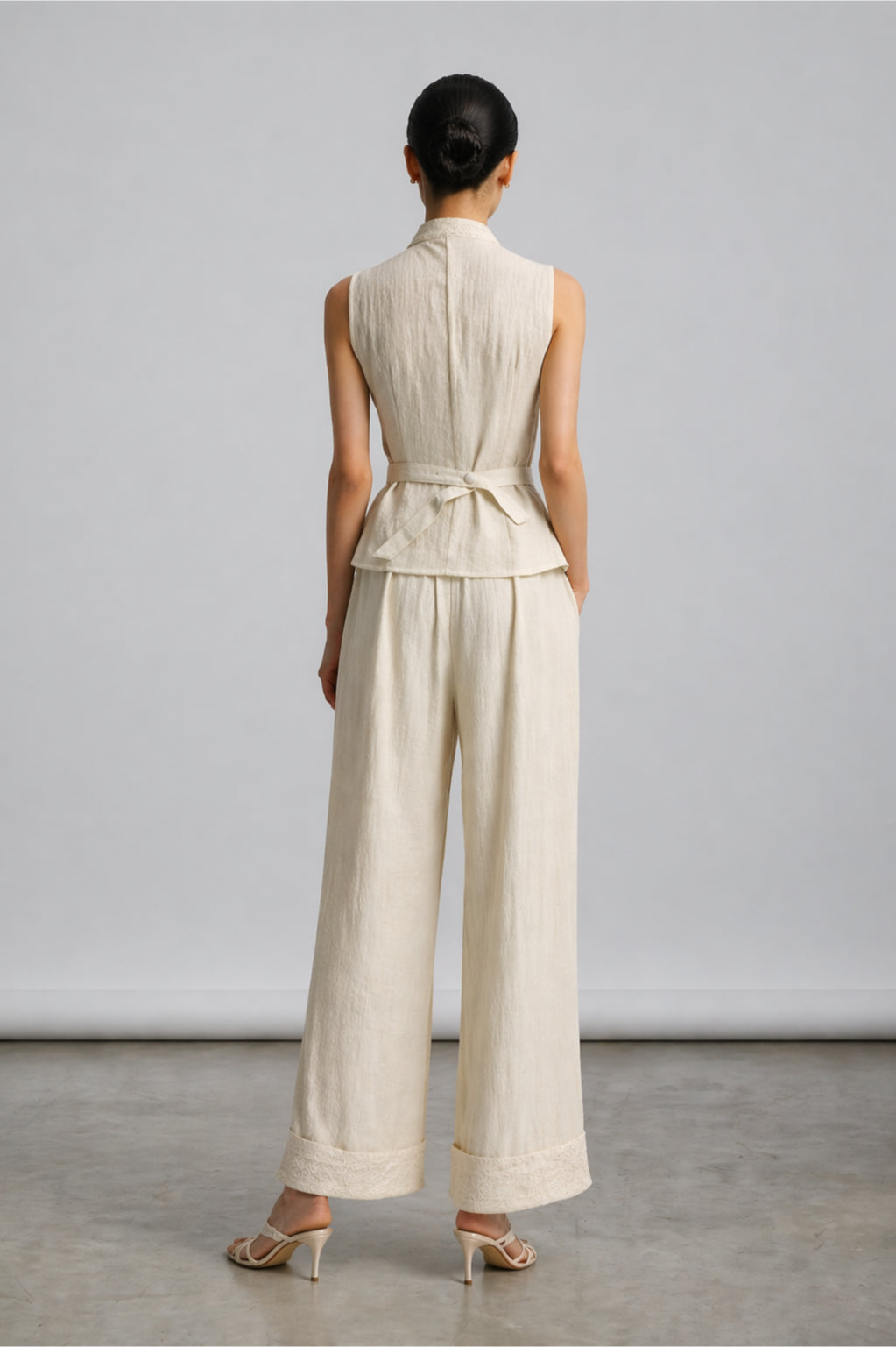 Woman wearing a beige sleeveless top and wide-leg pants against a plain background