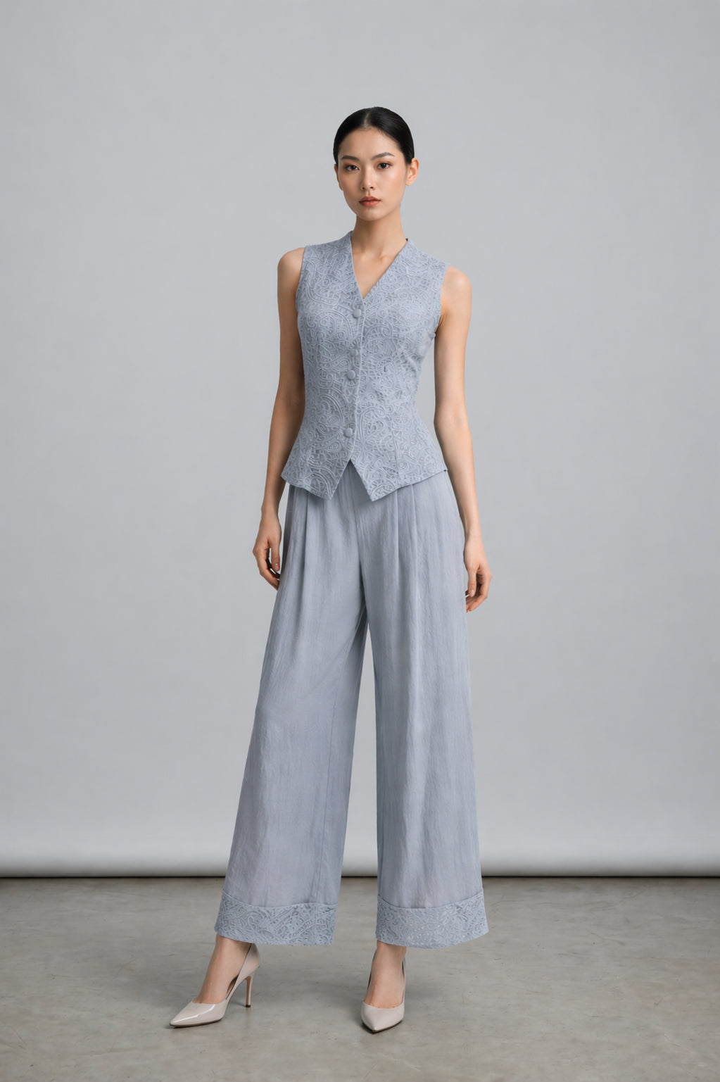 Woman wearing a light blue sleeveless top and wide-leg pants against a plain background