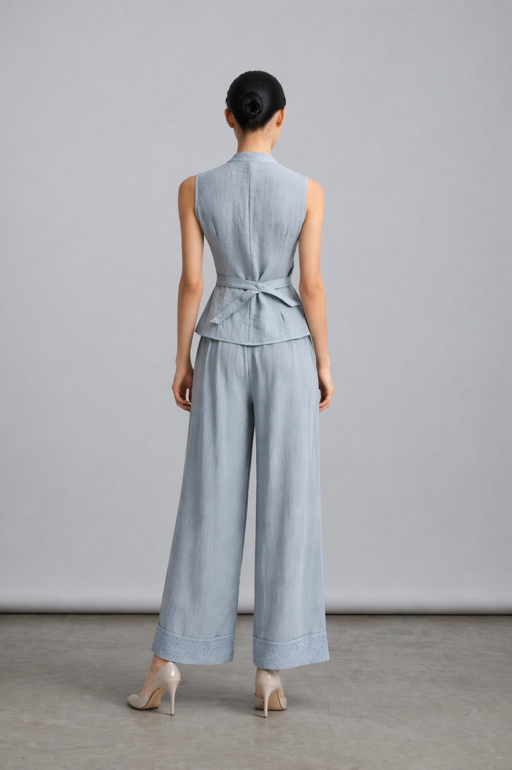 Woman wearing a light blue sleeveless top and wide-leg pants against a gray background