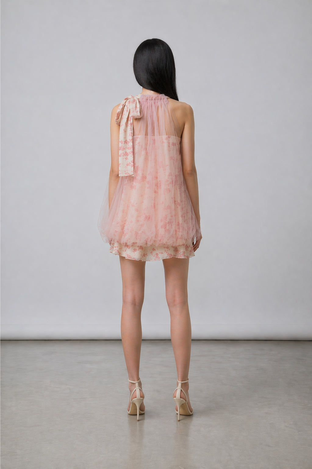 Woman wearing a pink dress with a bow detail on a plain background