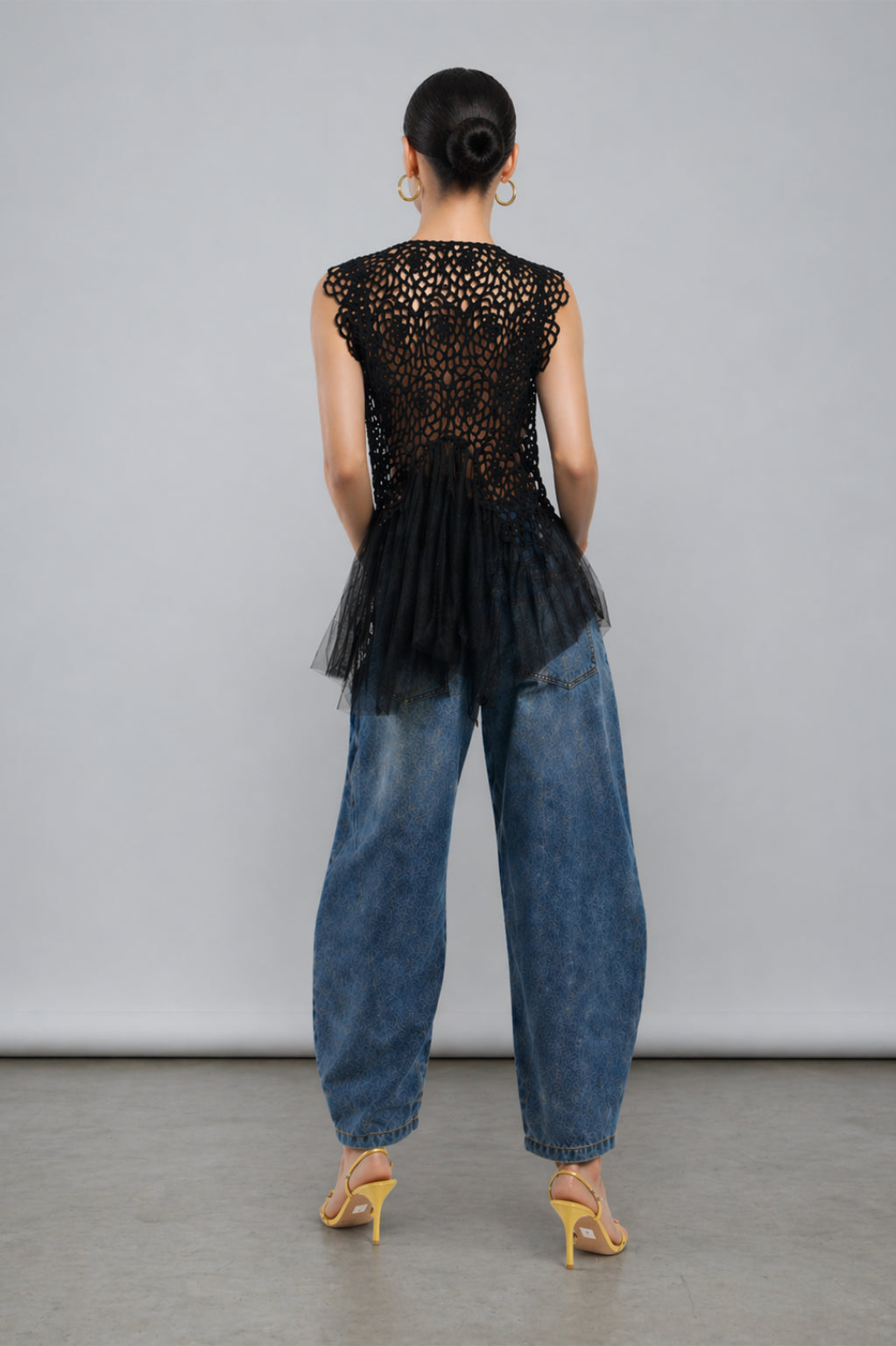 asian model wearing a black lace top and blue jeans from the back on a gray background