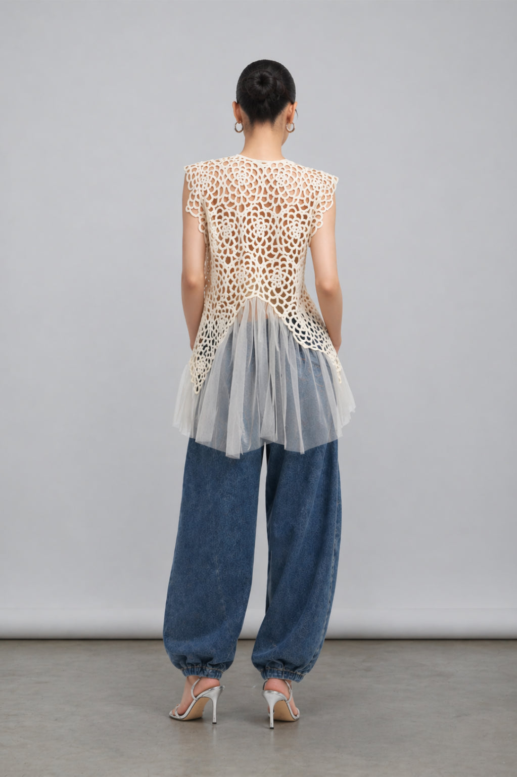 Person wearing a lace top and blue jeans with a sheer overlay against a gray background