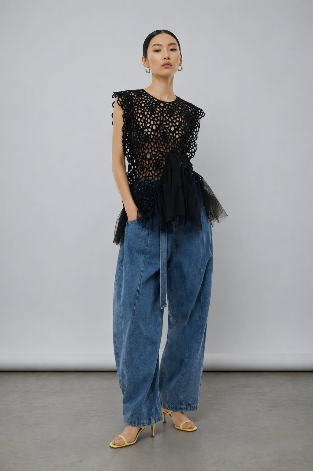 Woman wearing a black lace top and blue jeans against a gray background
