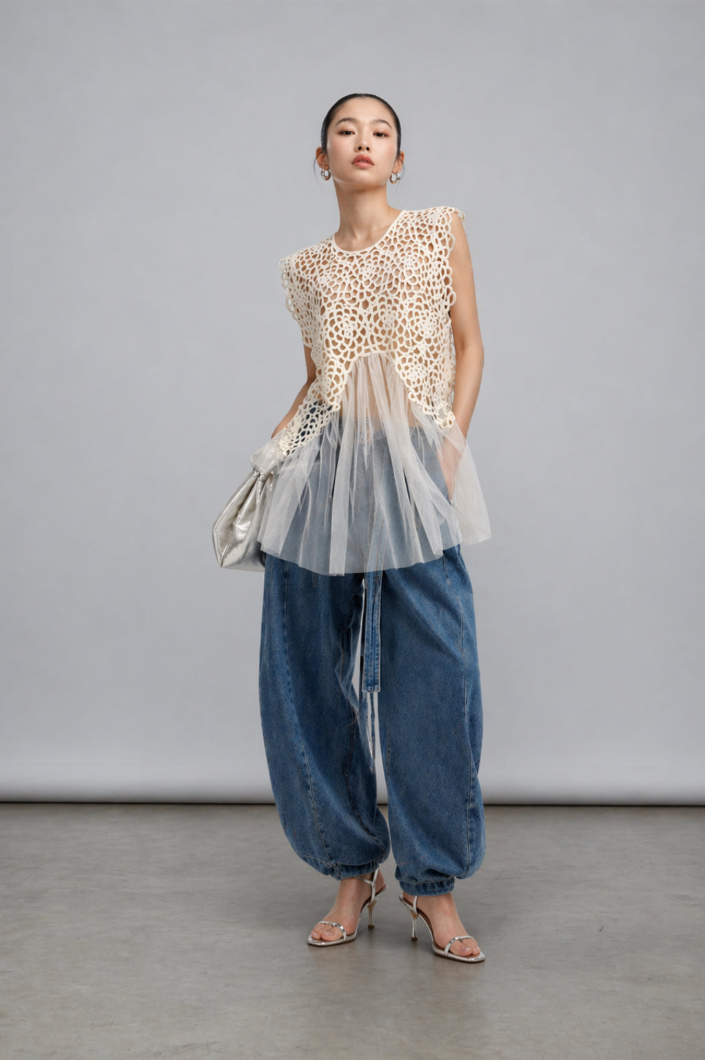 Woman wearing a lace top, cream color, and blue jeans against a gray background