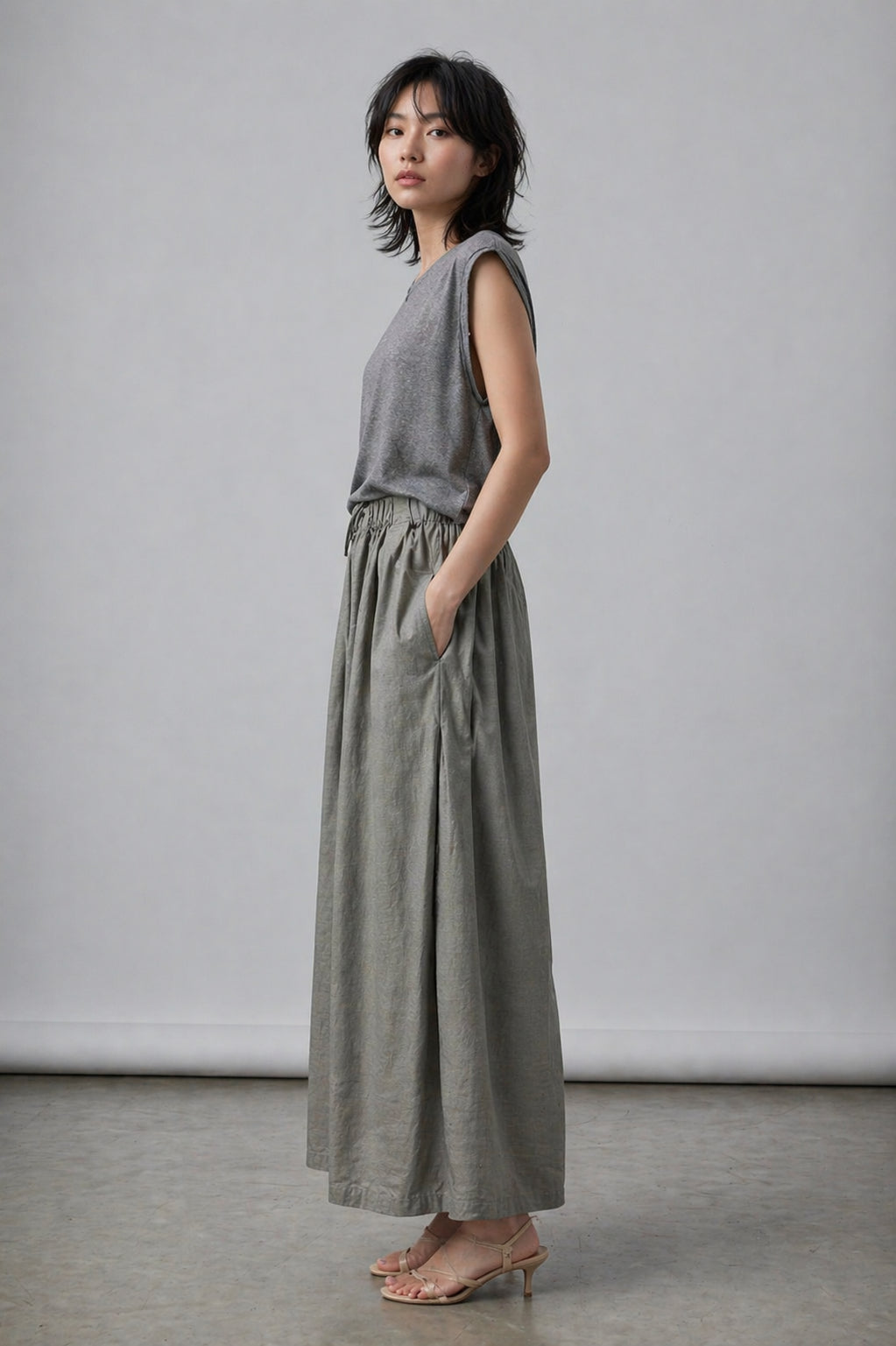 Woman wearing a gray sleeveless top and wide-leg pants against a plain background