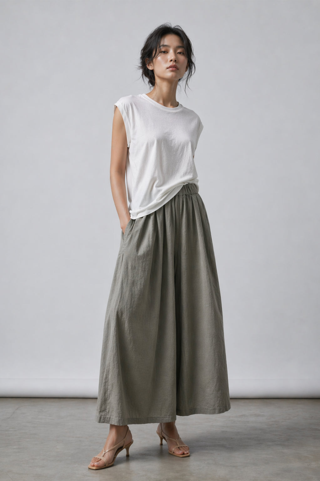 Woman wearing a white sleeveless top and long olive green skirt against a plain background