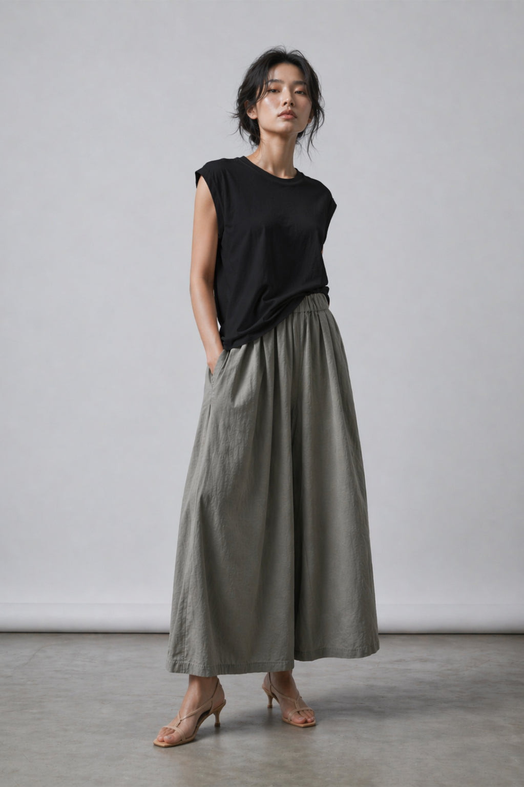 Woman wearing a black sleeveless top and gray wide-leg pants against a plain background