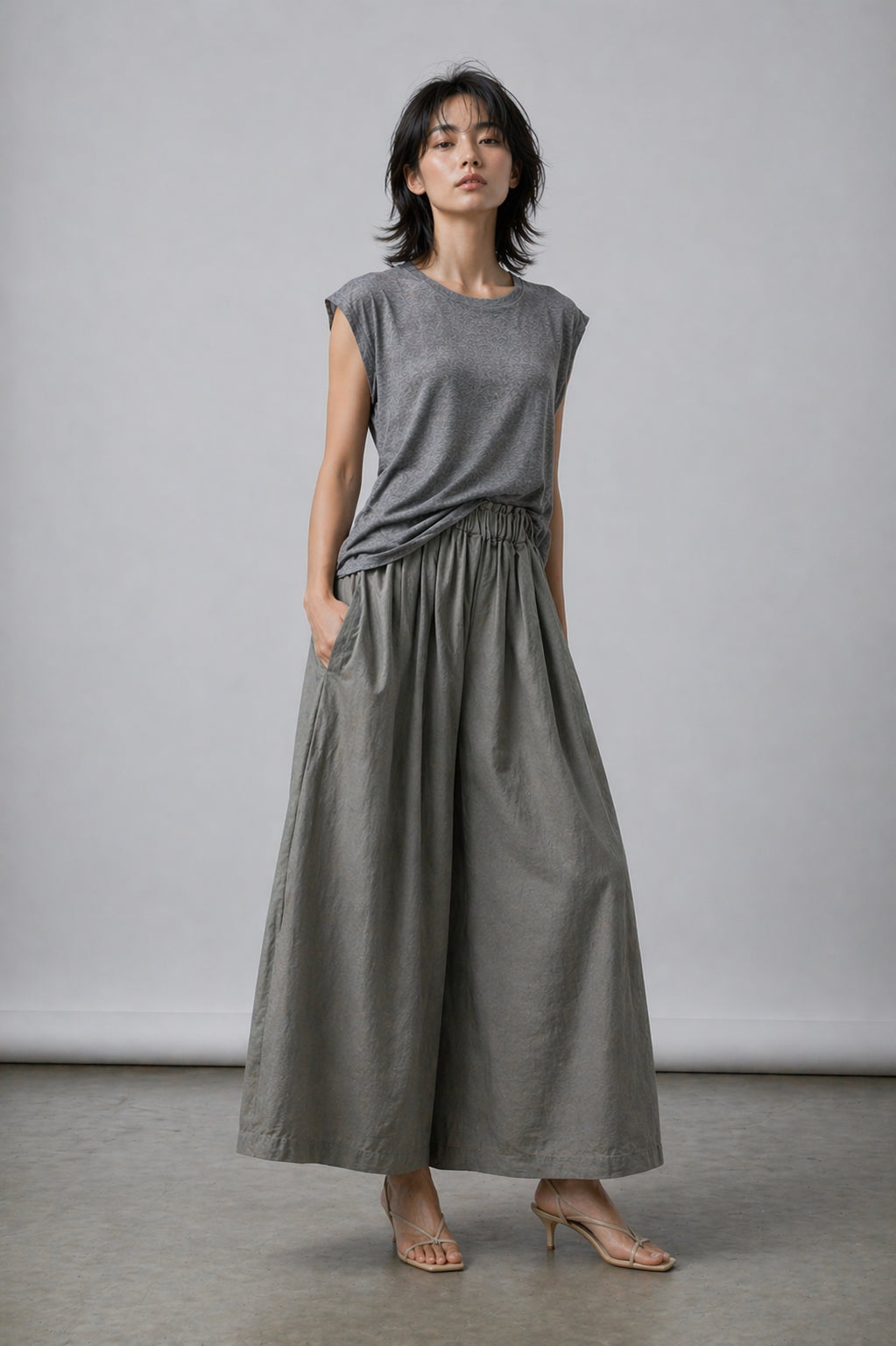 Woman wearing a gray sleeveless top and wide-leg pants against a plain background